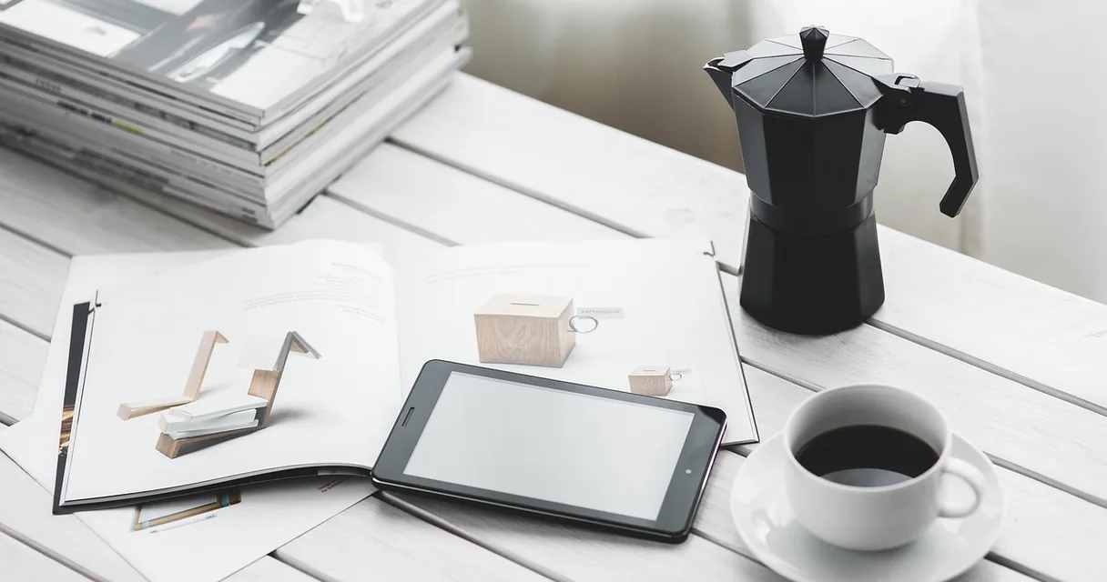 Tablet sobre uma mesa ao lado de uma xícara de café e revistas
