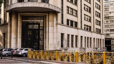 A imagem mostra a fachada de um edifício que abriga o INSS (Instituto Nacional do Seguro Social). O prédio é de estilo arquitetônico moderno, com uma entrada principal destacada por portas grandes e uma inscrição visível com as letras