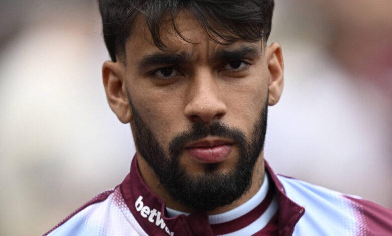 Um jovem jogador de futebol com cabelo escuro e barba, vestindo uma camisa de treino com as cores marrom e azul. Ele está olhando diretamente para a câmera com uma expressão séria. O fundo é desfocado, sugerindo um ambiente de estádio.