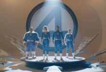 A imagem mostra quatro personagens em trajes azuis, em uma plataforma circular. Eles estão posicionados em uma pose heroica, com um grande símbolo do Quarteto Fantástico ao fundo. A iluminação destaca os personagens, criando um efeito dramático. O ambiente é moderno e minimalista, com elementos gráficos ao redor.