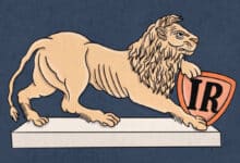 A imagem apresenta um leão em posição de alerta, com uma pata apoiada em um escudo. O leão é de cor clara, enquanto o escudo é laranja com as letras