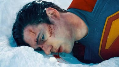 A imagem mostra um homem deitado na neve, vestindo um traje de super-herói com o símbolo de um