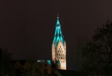 Der Turm des Paderborner Domes wird vor einem dunklen Nachthimmel farbig angestrahlt.